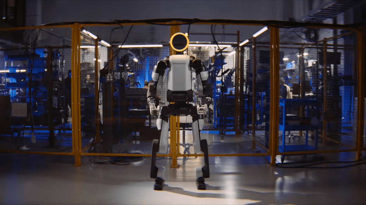 Sarı güvenlik bariyerleriyle çevrili bir atölyede duran insansı robot.